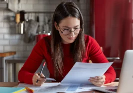 Mujer revisando documentos financieros en casa para mejorar su puntaje en Buró de Crédito, analizando reportes y pagos.