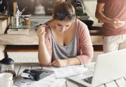 Mujer revisando cuentas y gastos del hogar con calculadora y laptop, concepto de finanzas personales y control financiero