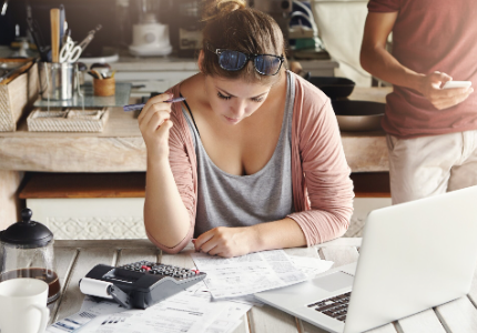 Mujer revisando cuentas y gastos del hogar con calculadora y laptop, concepto de finanzas personales y control financiero