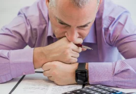 Hombre analizando deudas y opciones de préstamos personales con calculadora, evaluando tasas de interés y cuotas mensuales.