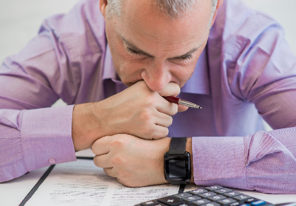 Hombre analizando deudas y opciones de préstamos personales con calculadora, evaluando tasas de interés y cuotas mensuales.