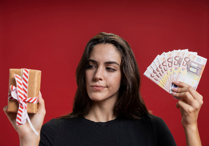 Mujer comparando una caja de regalo y dinero en efectivo, simbolizando la decisión entre gastar o pedir un préstamo a comienzos de año, fondo rojo.