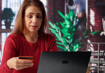 Pessoa preocupada usando notebook e segurando cartão após empréstimo aprovado ser cancelado pelo banco