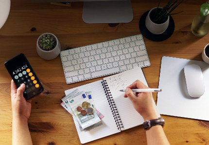 Pessoa calculando despesas com dinheiro e calculadora sobre mesa, representando controle financeiro e planejamento de gastos