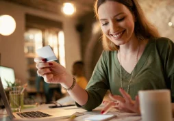 Mulher usando aplicativo bancário no celular e cartão para movimentar conta e melhorar chances de conseguir empréstimo