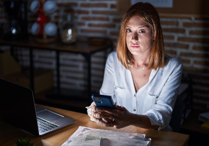 Mulher preocupada usando celular à noite ao lado de notebook, representando bloqueio de crédito e dificuldades financeiras