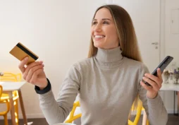 Mulher sorrindo segurando cartão de crédito e celular, representando controle financeiro e melhora no score de crédito