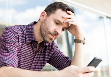 Homem preocupado olhando celular ao ver score de crédito travado, representando dificuldade em aumentar a pontuação